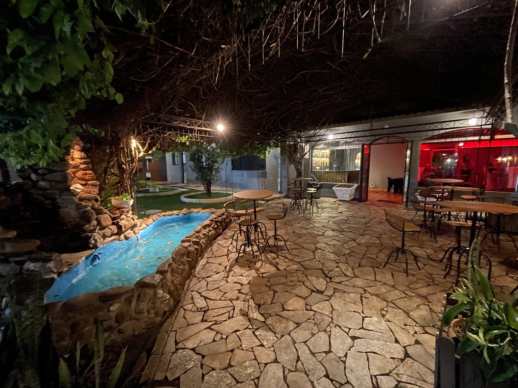 Jardim externo da Enigma com fonte, mesas e iluminação noturna